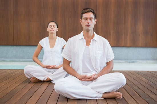 Peaceful couple in white sitting in lotus pose together in health spa